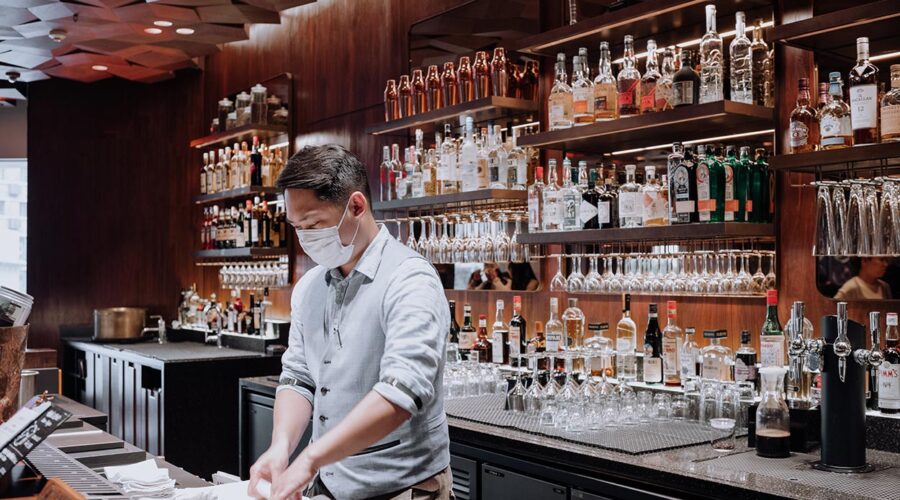 a bartender in mask cleans behind the bar