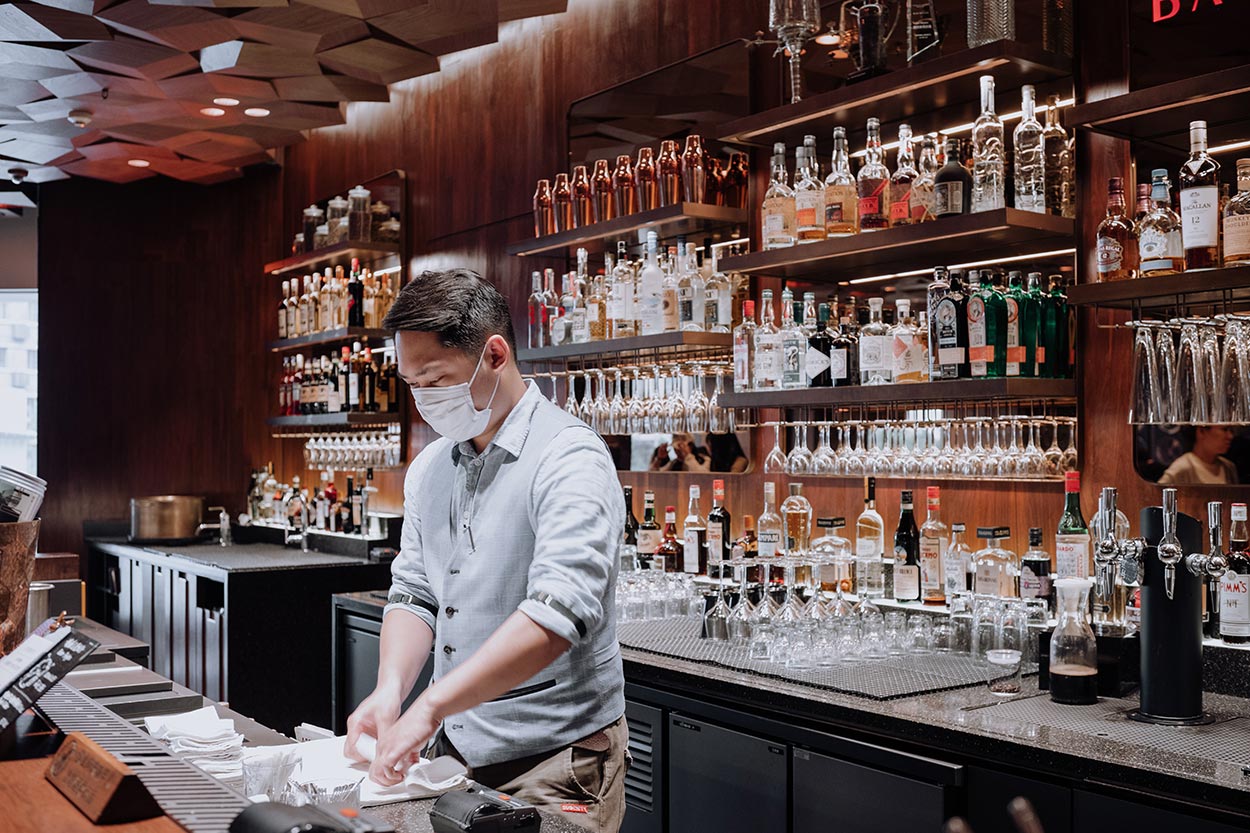 a bartender in mask cleans behind the bar