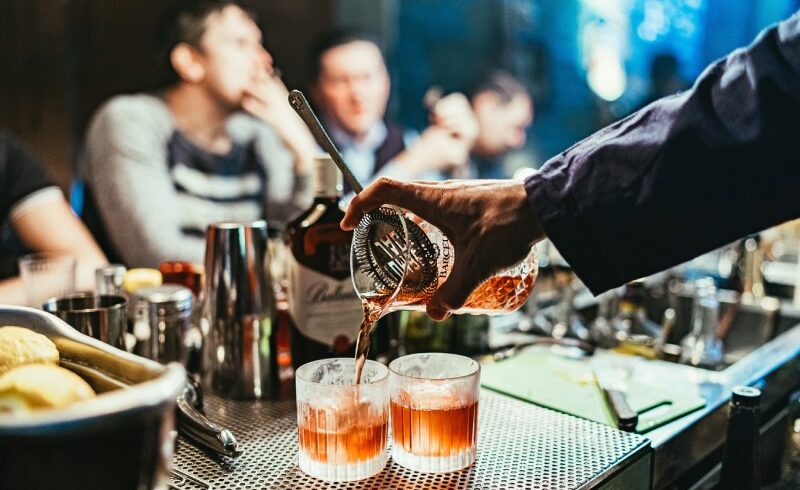 A bartender using a hawthorn strainer to pour drinks for waiting customers